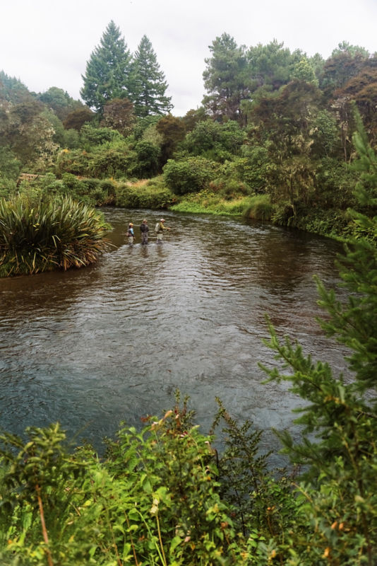 Three anglers picking their way along a steep bank of a river.