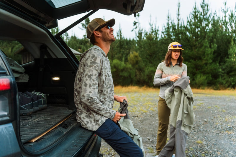 A man sitting in a back of a car wearing a camo printed sun protection hoodie.