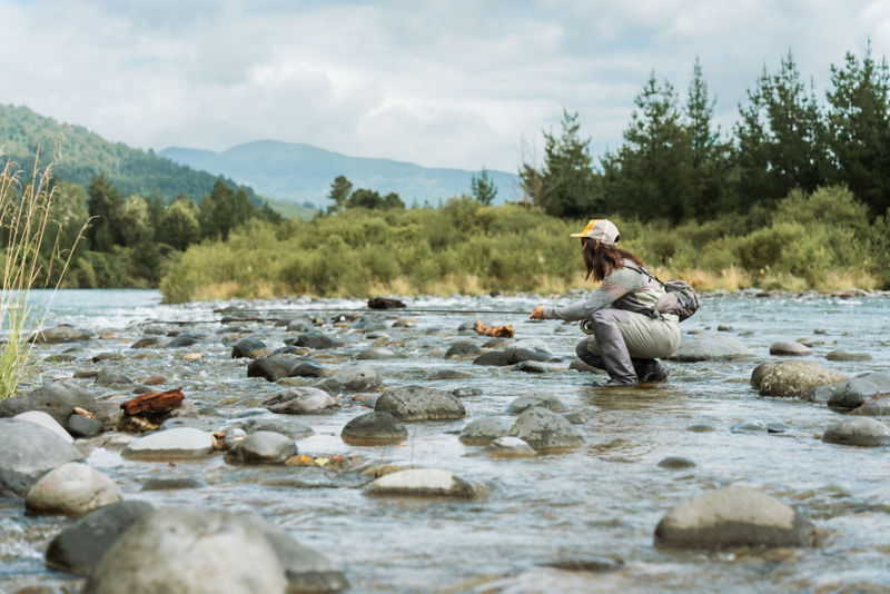 An angler crouches in a a shallow stretch of a rocky river.