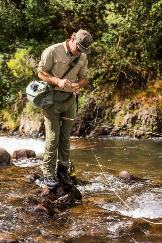 An angler standing on rocks tying a fly to his line.