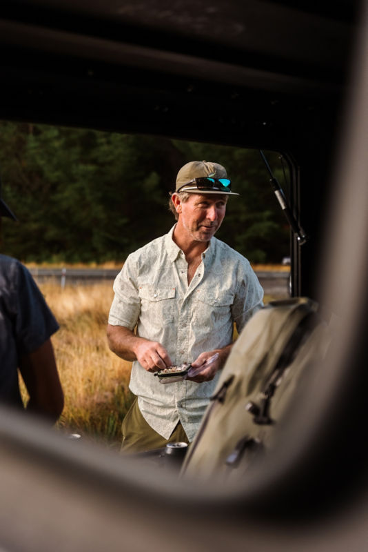 An angler wearing a light button down shirt and an olive hat choosing a fly.