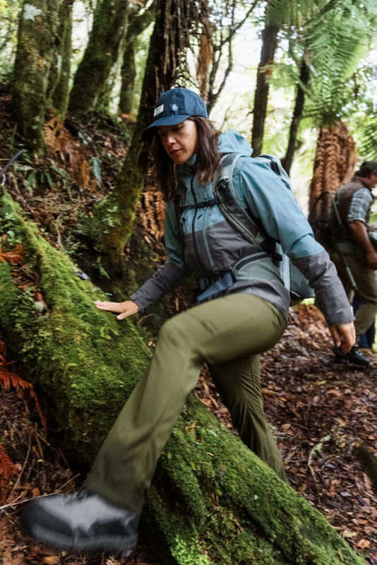 A person wearing a PRO fishing jacket and backpack picks her way across a steep slope.