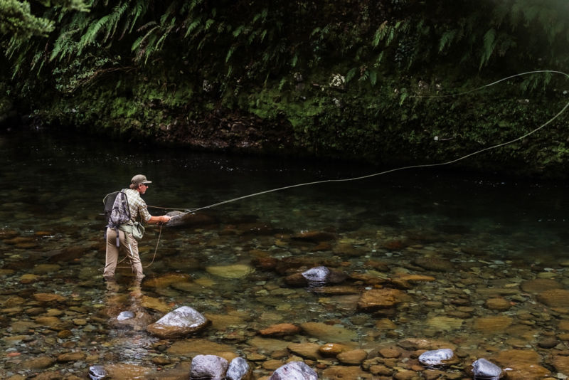 An angler casts from knee deep in a rocky stream.