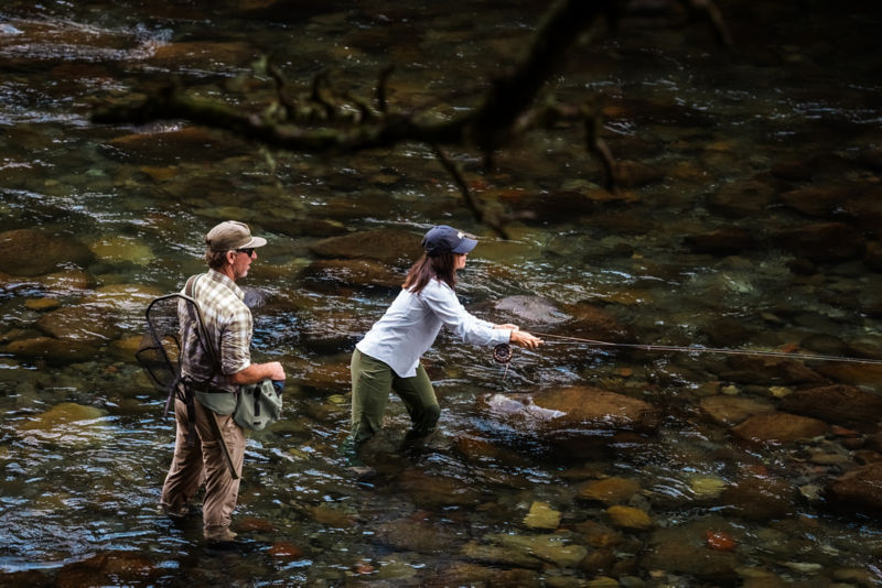 A guide talks through a cast with a customer from knee deep in a river.