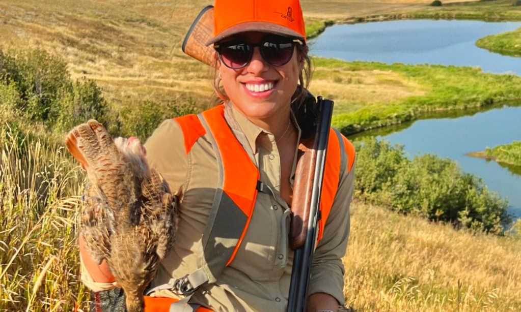A wingshooter in a blaze orange ball cap smiles as she shows off her bird.