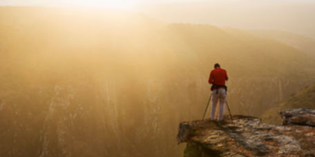 A photographer with a tripod camera at the top of a cliff.