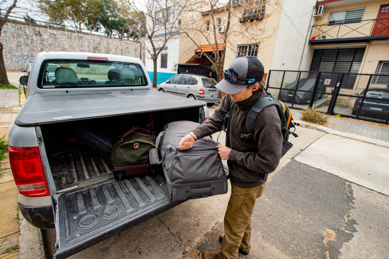 An adventurer packs the back of a pick-up truck with a variety of luggage.