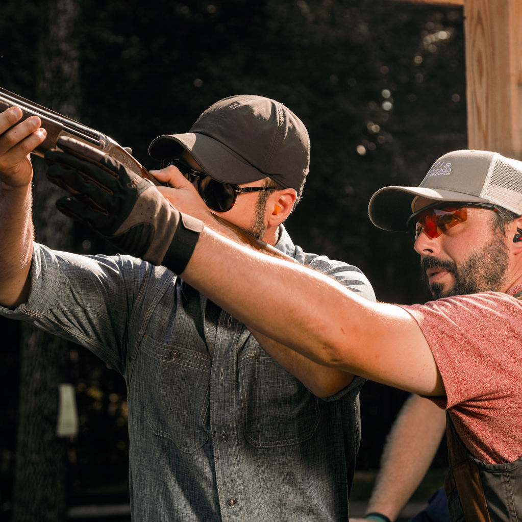 A student aims their shotgun while an instructor watches from behind them