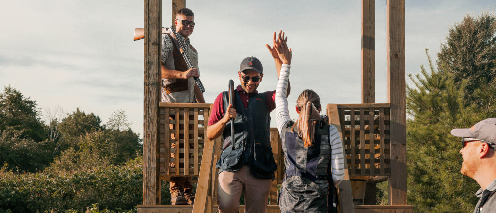 A clays shooter high fives another person while passing on the stairs to the shooting stand