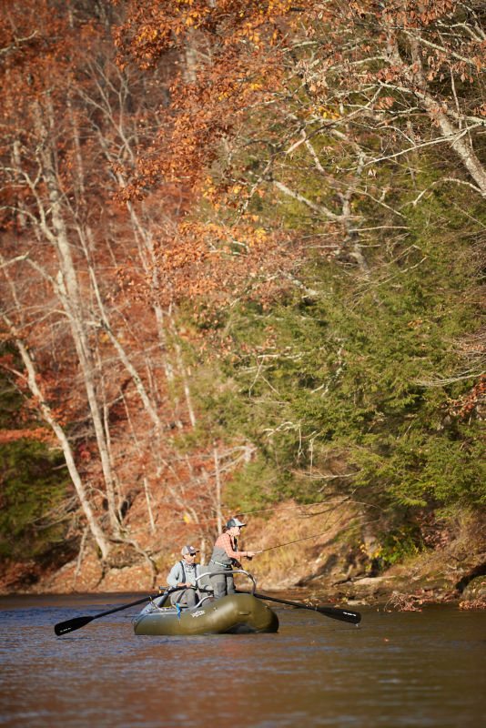 An angler leans into her cast from the front of a raft.