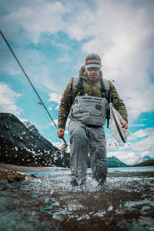 A man in PRO Waders walks up a rocky river.