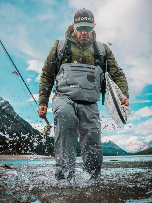 A man in PRO Waders walks up a rocky river.