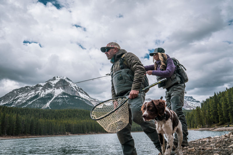 Two people fishing with snow capped mountains in the background