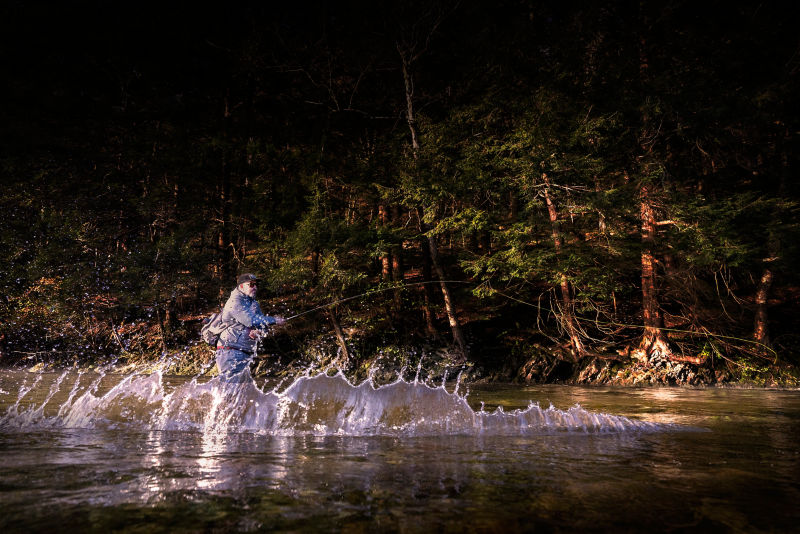An angler casts two-handed in a shallow river.