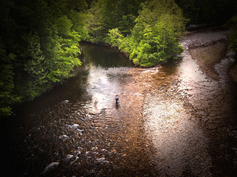 Seen from above, an angler wades in the shallows and casts into the deeper part of the river.