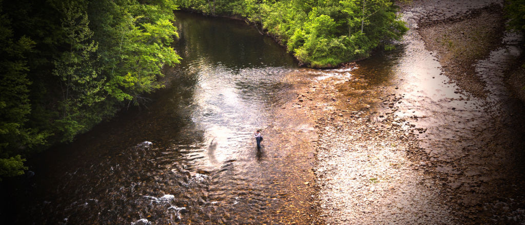 Seen from above, an angler wades in the shallows and casts into the deeper part of the river.