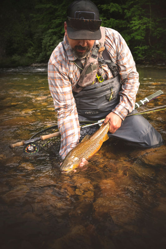 Man holding a large brown trout in rapidly moving water.