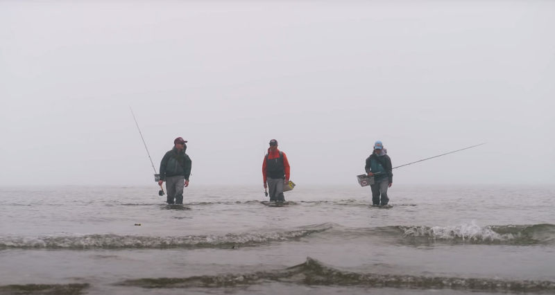 Three anglers with full gear wading in the ocean