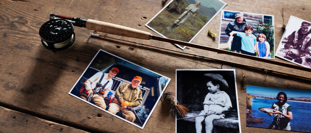 Old photos lay around a bamboo fly rod on a rough wooden table