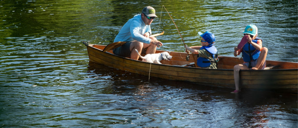 The CEO of Orvis, Simon Perkins teaches his small son the finer points of fly fishing in a wooden canoe.
