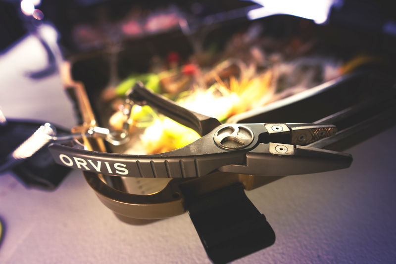 A pair of Orvis pliers rests on a fly box.
