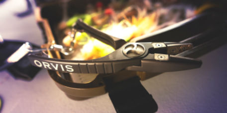 A pair of Orvis pliers rests on a fly box.