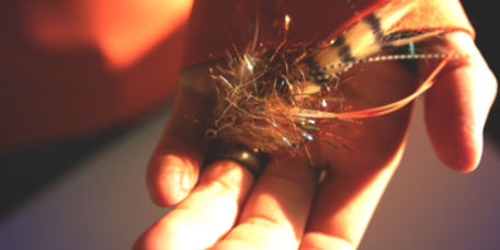 An angler holds a large streamer fly in the palm of their hand.
