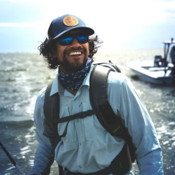 Angler with mens PRO Hybrid Shirt smiling against a backdropped ocean.