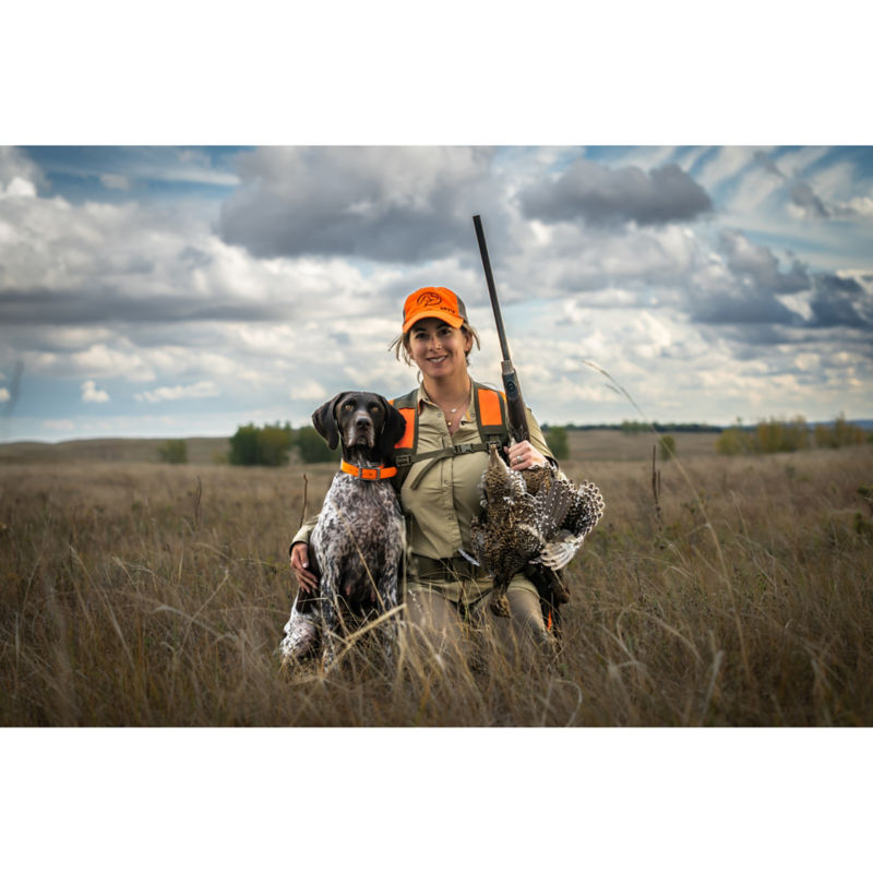 Kat Pippit kneels in a field of dry grass with her dog.