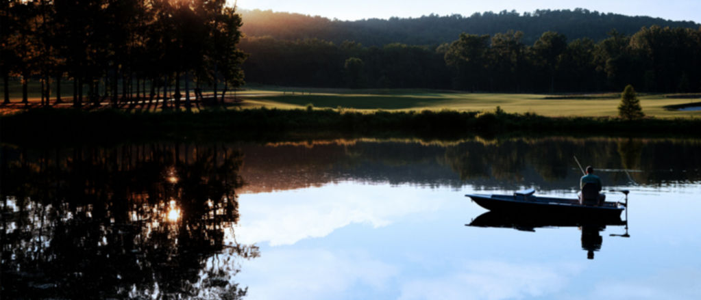 A johnboat floats on a still lake as the sun rises in the background