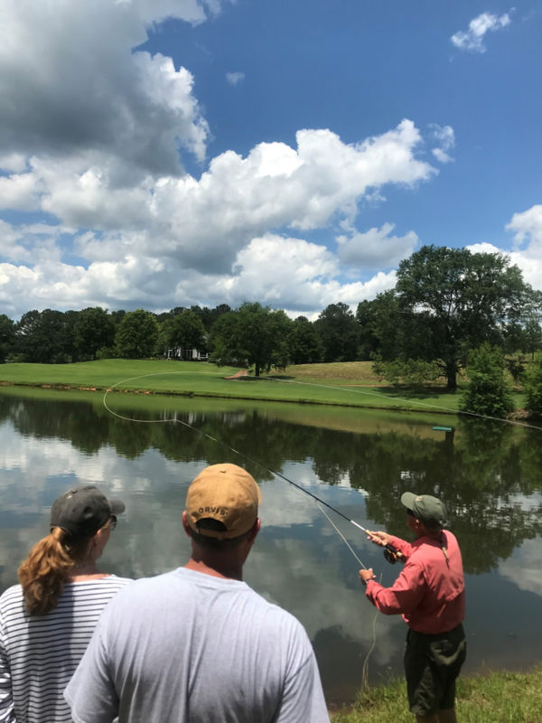 An angler teaches two students a cast