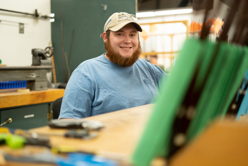 A smiling young man with an orange beard sits at a work desk