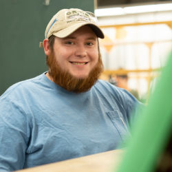 A smiling young man with an orange beard sits at a work desk