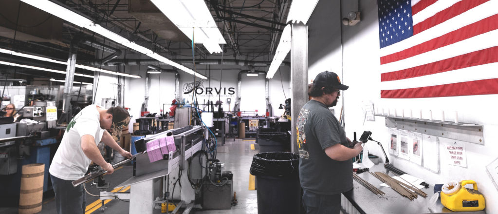 Several people work over complex machinery inside the Orvis Rod Shop