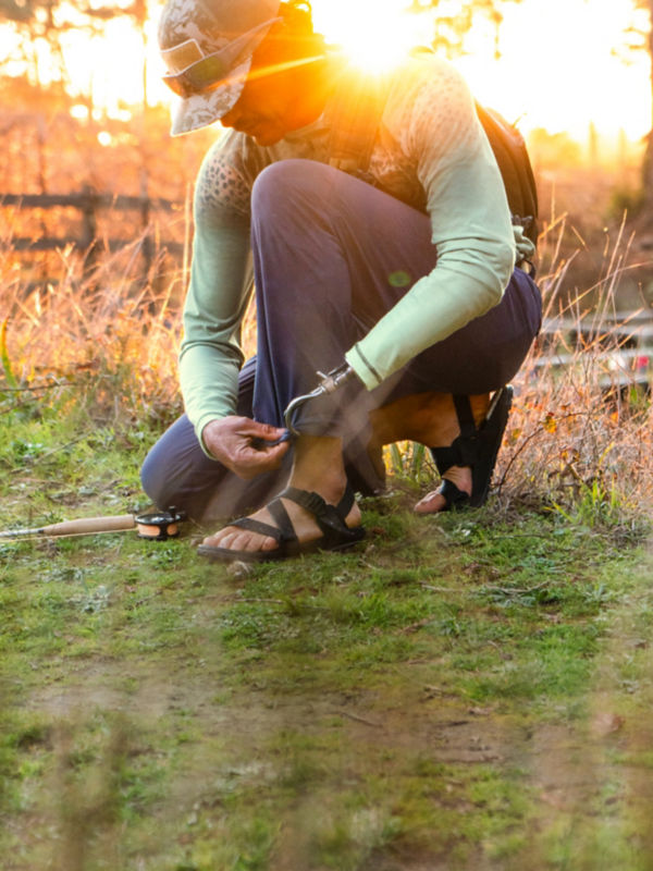 A hiker sits on a wooden deck offering a water bottle to someone off camera.