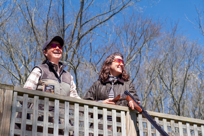 A shooting instructor and student smile in the bright sunlight.