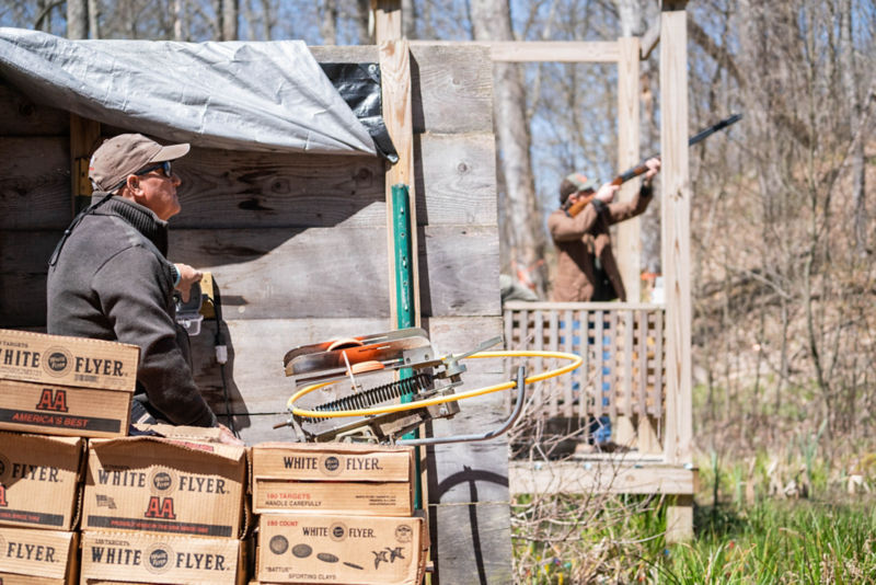 One person runs the clays machine while in the background a shooter stands ready.