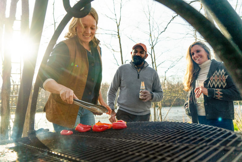 Two bystanders watch as another person grills peppers on a cold fall day.