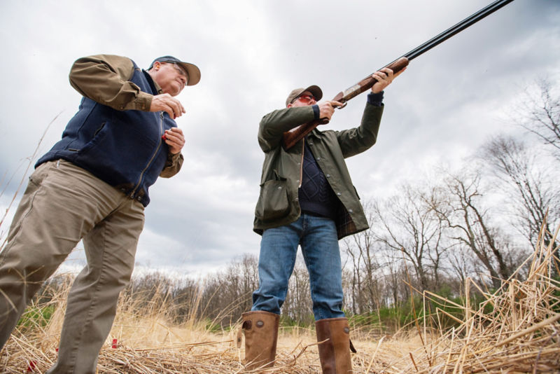 A hunter lifts his shotgun to his shoulder.