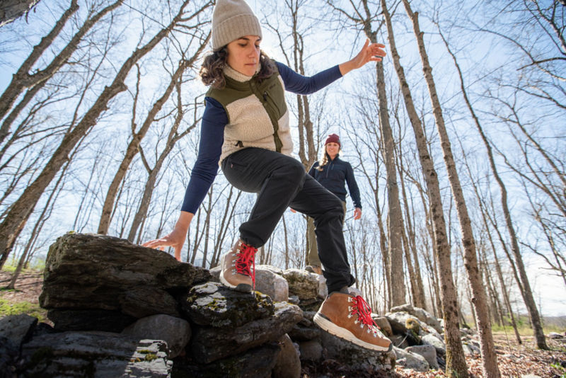 Woman hoping over a log in black JQD with sherpa vest and beanie on