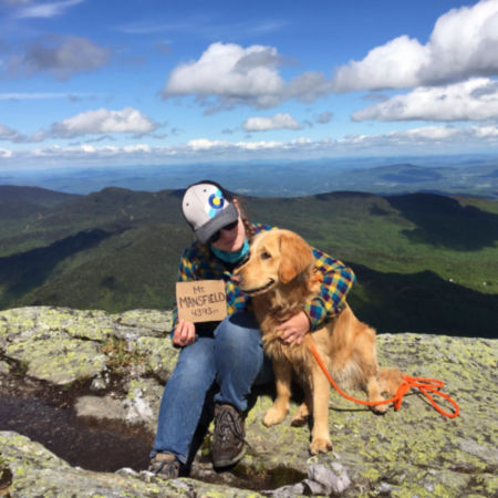 A young woman and her dog sitting on the summit of a mountain