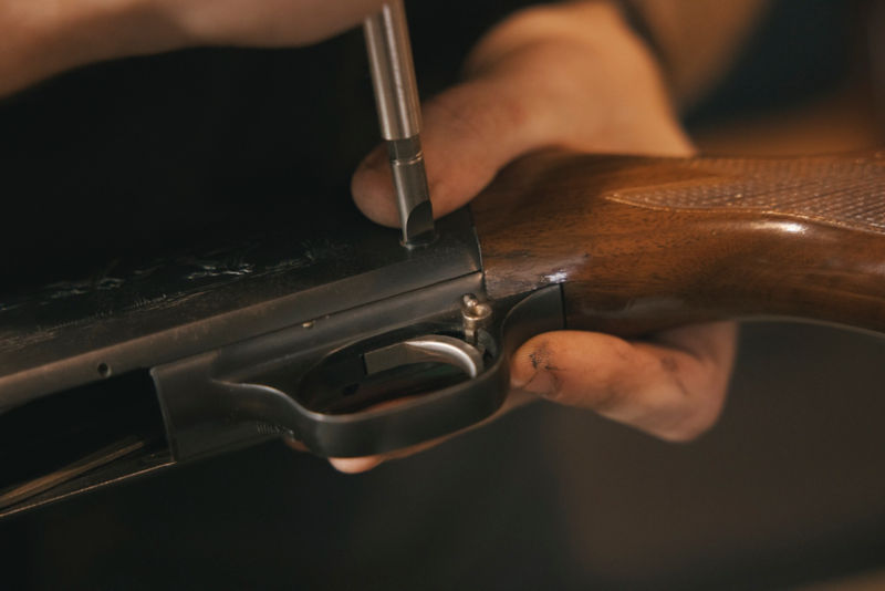 A gunsmith screws a connector to a shotgun.