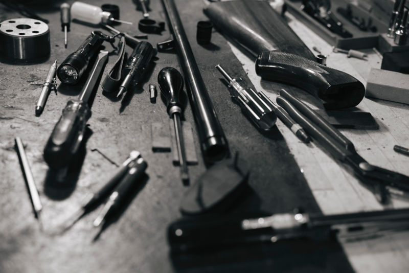 A black and white image of a shotgun stock and tools on a work surface.