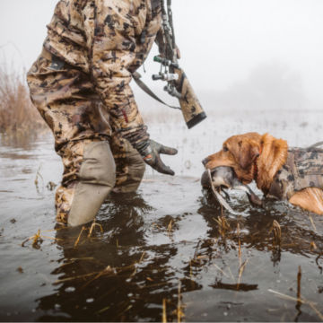 A hunter retrieves a duck from his dog.