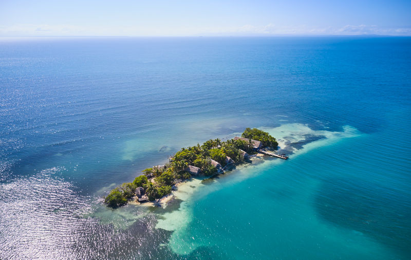 A small green tropical penninsula juts into the middle of a turquoise sea.