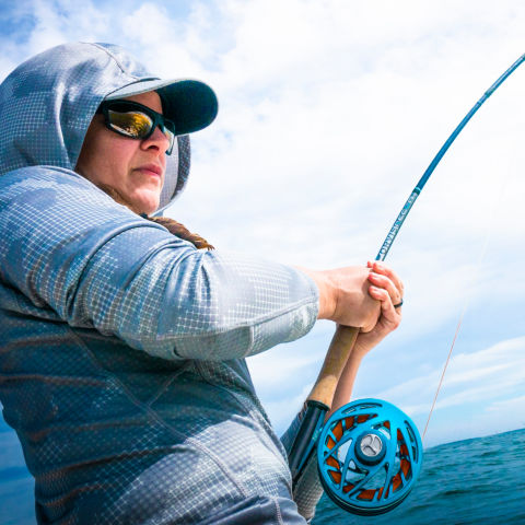 An angler in sunglasses and PRO hoodie fights a fish on the line