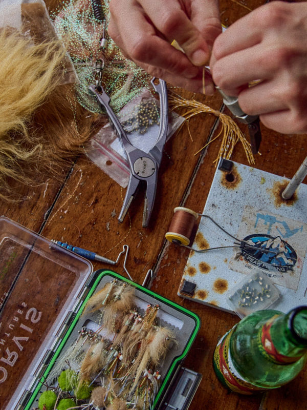 A close-up of two hands tying a fly with supplies on a wooden table.