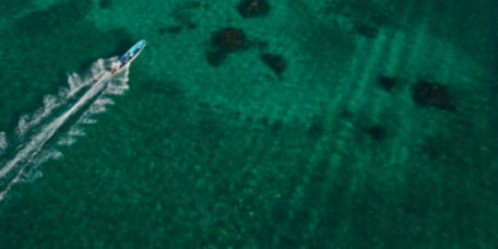 A drone-view of a boat speeding through emerald green waters.