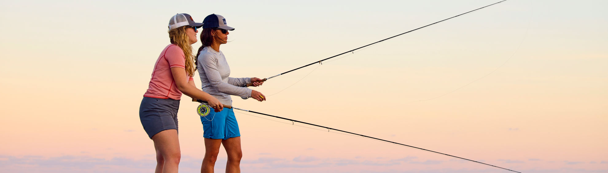 Two women fly fish off the end of a dock