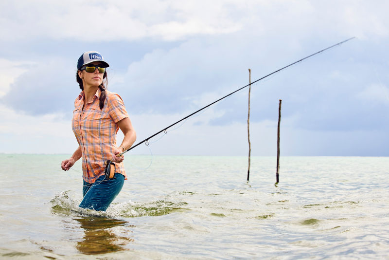 A woman shoots her rod in the surf.